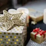 A picture focused on a golden star. Some wrapped gifts and candles are also there.