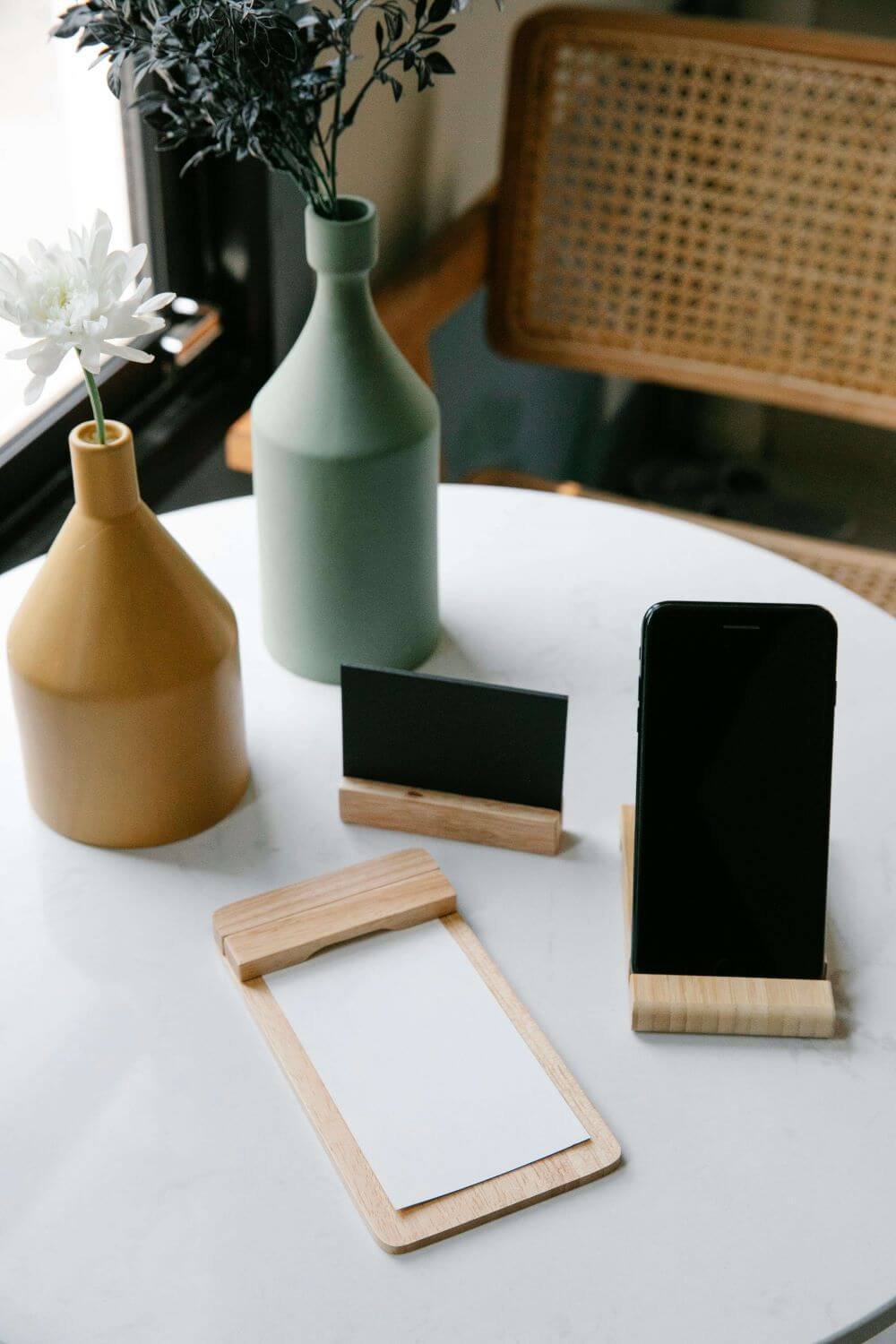 On a table two flower vase with flowers, one phone stand with phone, and another notepad are kept.