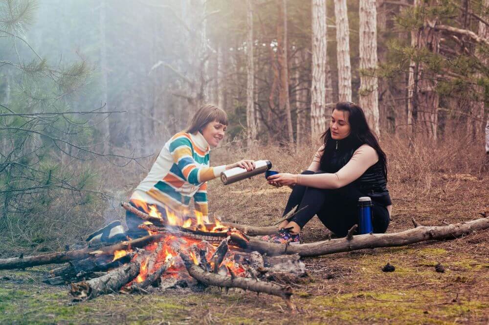 A hangout or picnic in a park between two girls. One is pouring tea to another.