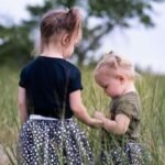 Two little girl in a field. The older one is holding hands of the little girl's.