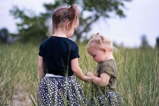 Two little girl in a field. The older one is holding hands of the little girl's.